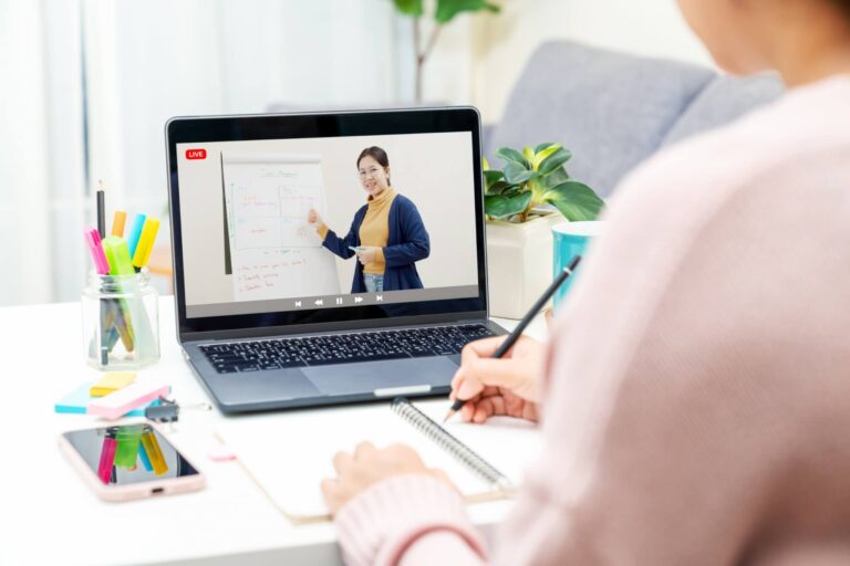 Frau schaut auf einen Laptop Screen, wo eine Frau etwas erklärt. Das ist die Einleitung zum Blogpost 'Führungskräfte virtuell onboarden'