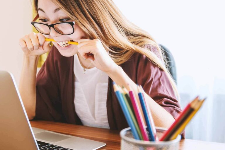 Frau sitzt am Laptop und beißt auf einen Stift. Das ist das Titelbild für den Blogpost 'Mitarbeiter entwickeln, aber richtig'