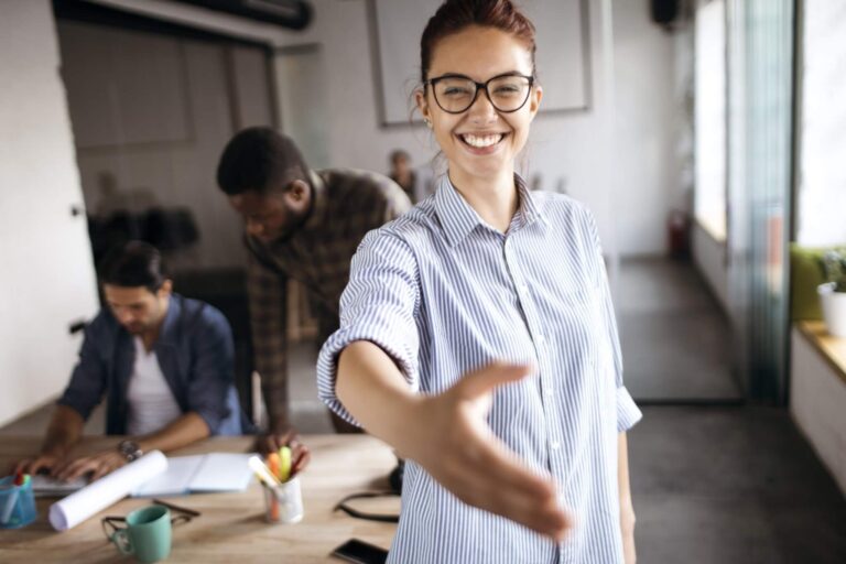 Eine Frau lächelt und streckt die Hand aus zur Begrüßung. Das ist die Einleitung zu einem Artikel über Onboarding.